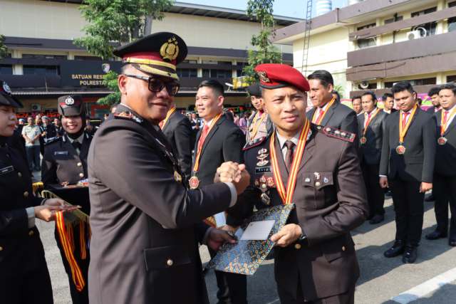 Kapolrestabes Medan, Kombes Pol. Dr. Gidion Arif Setyawan memberikan penghargaan kepada salah seorang personel pada puncak HUT Bhayangkara ke-79 yang digelar di halaman Markas Polrestabes Medan, Selasa (1/7/2025).